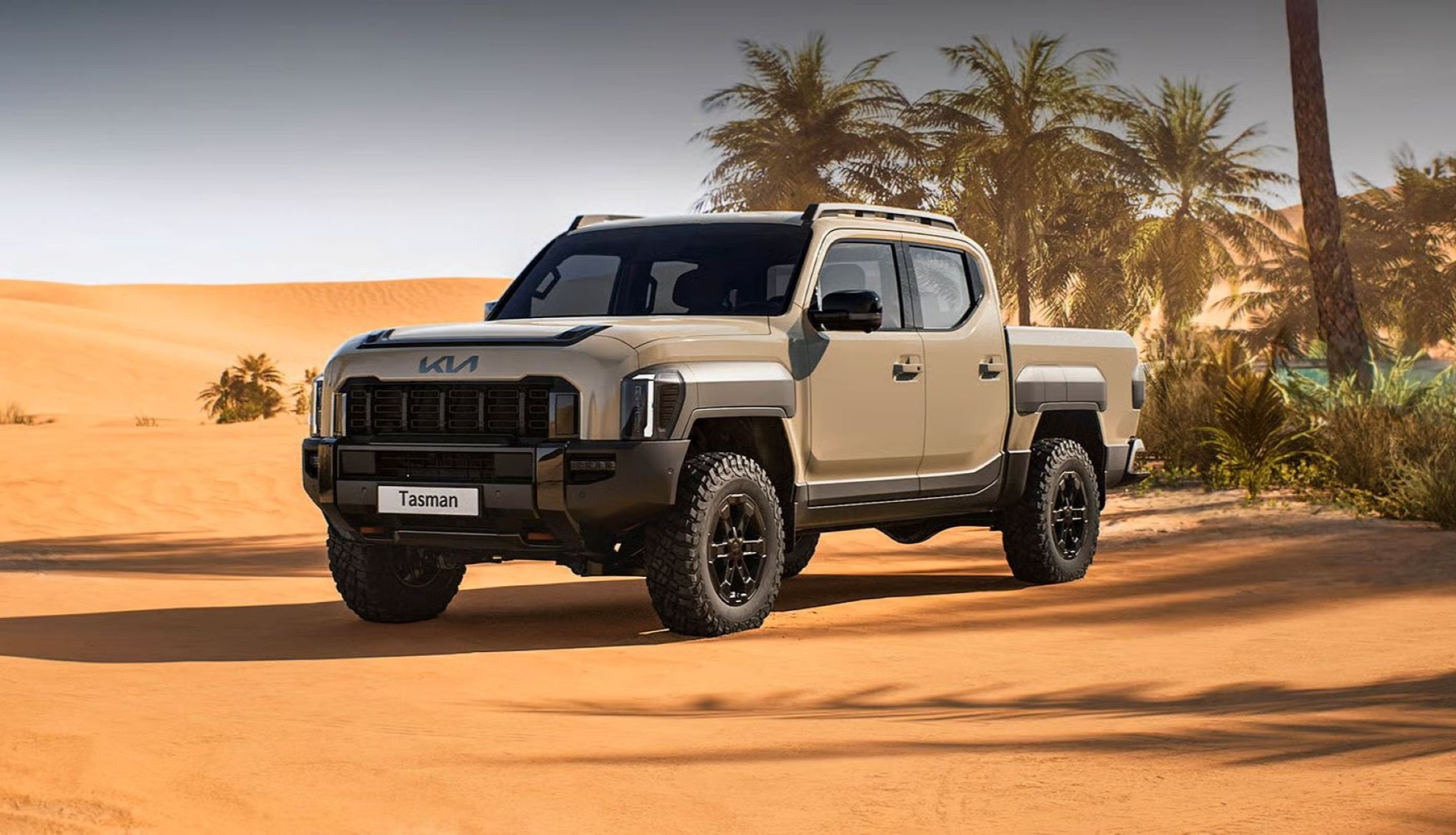A tan-colored Kia Tasman double-cab pickup truck parked on sand tracks in a desert landscape, with sand dunes and palm trees visible under a clear sky in the background.|Arabwheels.ae